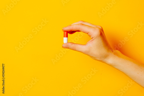 Female hand hold pill on yellow background