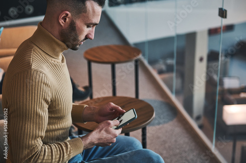 Multitasking young Middle-Eastern man using mobile phone, browses websites and books hotel while waiting the flight in a VIP lounge of international airport departure terminal photo