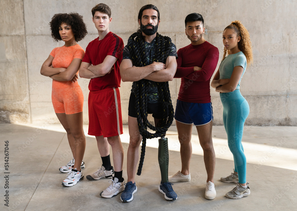 portrait of serious multiracial friends in sportswear standing together in a gym, in the center man with a beard, and leg with an amputation prosthesis.