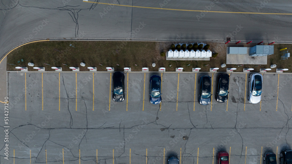 A direct overhead aerial view above a Tesla Supercharger station, cars are seen parked, charging during the day.