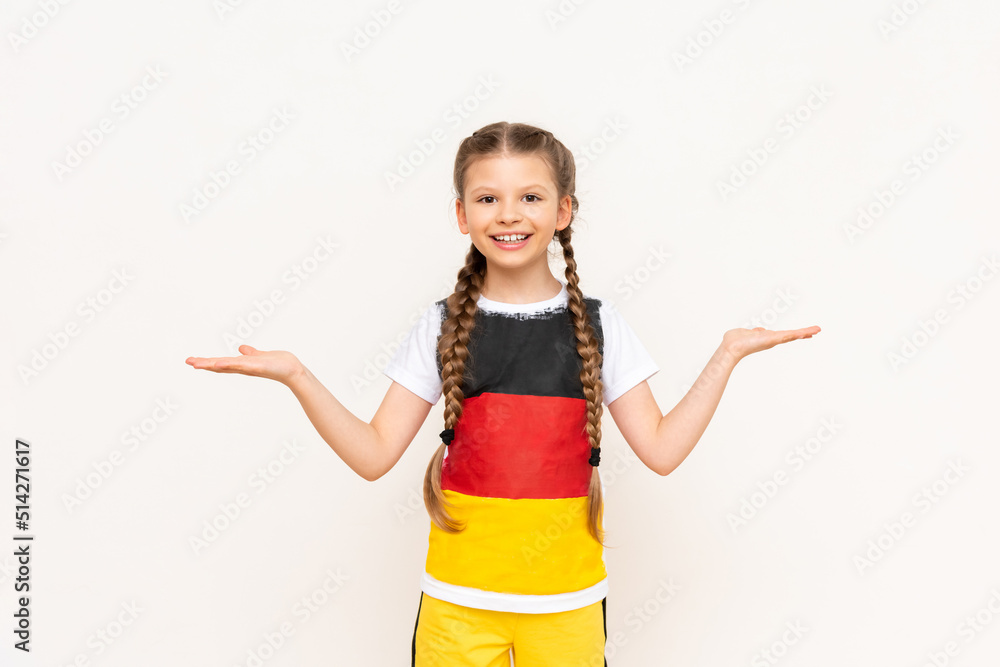 A little girl with a German flag on a T-shirt, with long hair in pigtails, holds your advertisement on a white isolated background on her palms. Language courses. Copy space. A little girl with a German flag on a T-shirt, with long hair in pigtails, holds your advertisement on a white isolated background on her palms. Language courses. Copy space.