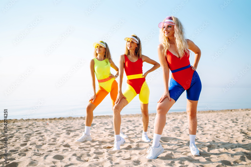 Beautiful women in swimsuits are dancing on the beach. Three woman are training in the morning. Fitness, training, aerobics and people concept. Active sport.