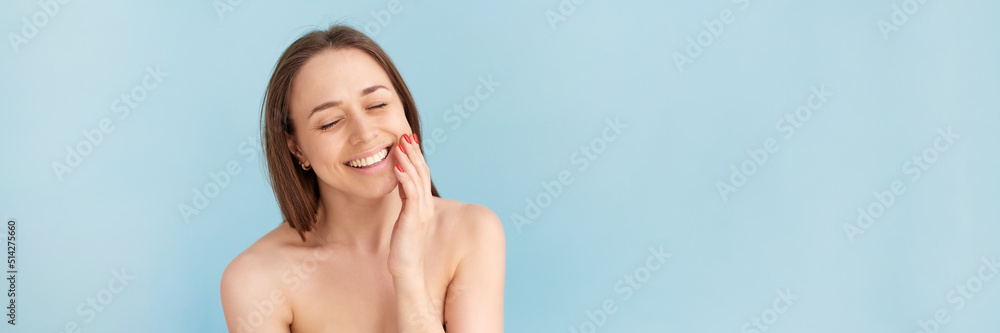 Smiling woman touching her face against a blue background. Natural beauty concept, happy woman. Web banner. Smiling woman touching her face against a blue background. Natural beauty concept, happy woman. Web banner.