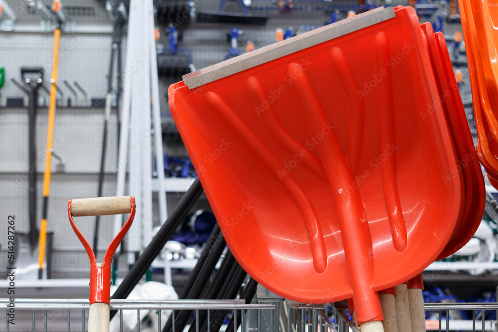 Orange plastic shovels for snow in a supermarket on the background of shelving.