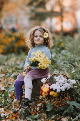 beautiful curly little girl in blue shirt in park with flowers at fall time, autumn, health, card, banner