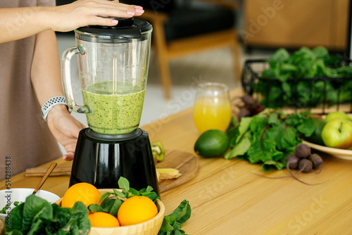 Fototapeta Naklejka Na Ścianę i Meble -  Woman preparing tasty green smoothie in kitchen, close up blender process, healthy diet detox concept