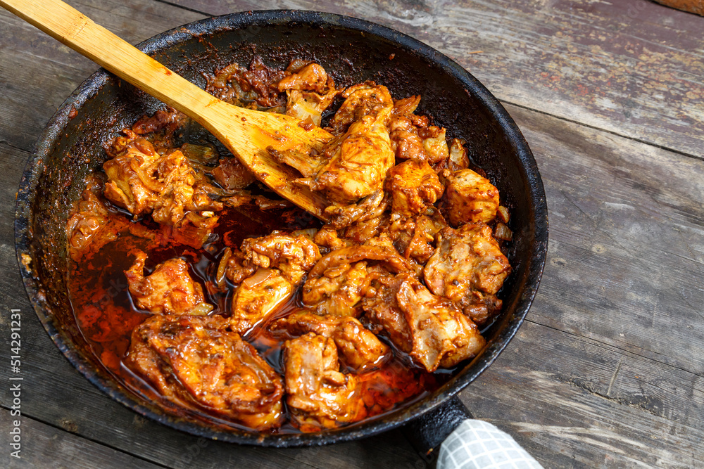 Fried chicken with spices in a frying pan with a wooden spatula on a dark table. Fried chicken with spices in a frying pan with a wooden spatula on a dark table.