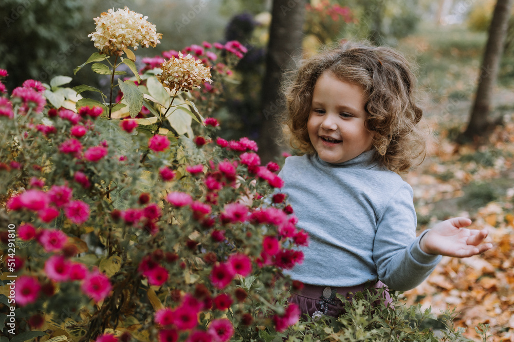 adorable curly little girl in blue shirt in park with flowers at fall time, autumn, health, card, banner adorable curly little girl in blue shirt in park with flowers at fall time, autumn, health, card, banner