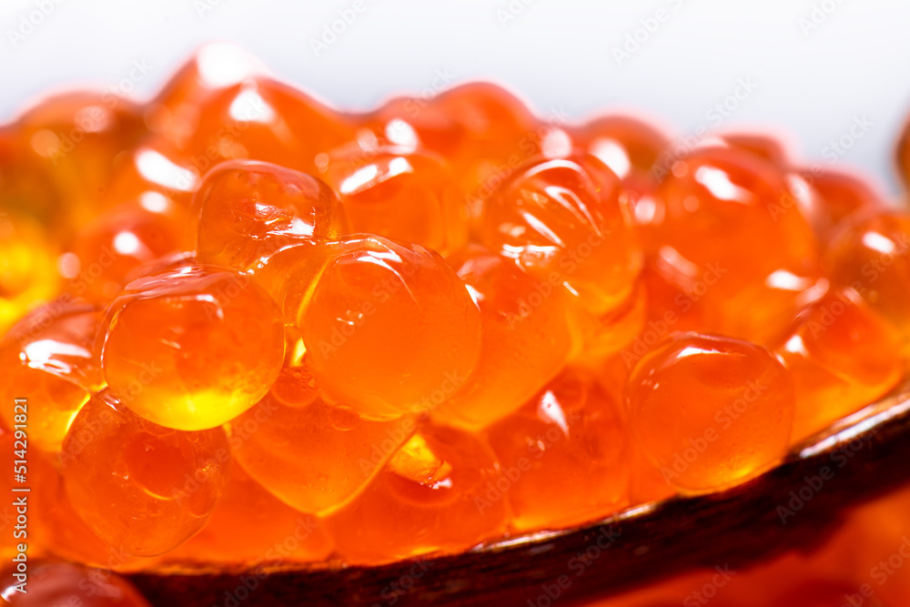 Orange beautiful caviar on wooden spoon on white blank background illuminated by white light. Orange beautiful caviar on wooden spoon on white blank background illuminated by white light.