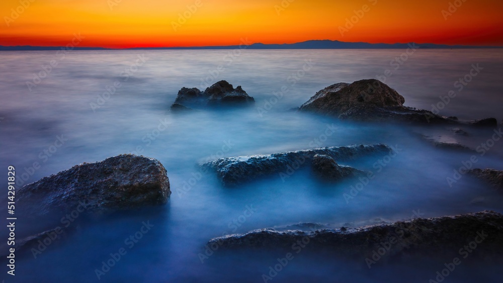 Widok skał oblewanych przez morze o wschodzie słońca przy kolorowym niebie - obrazy, fototapety, plakaty 