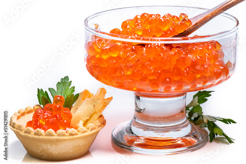 Red caviar in tartlet with oil and green herbs. Delicious and expensive caviar in glass cup with wooden spoon inside decorated with green parsley on bottom.