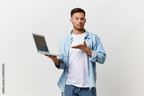 Serious friendly tanned handsome IT professional man in casual basic t-shirt point hand at laptop posing isolated on white studio background. Copy space Banner Mockup. Electronics repair concept