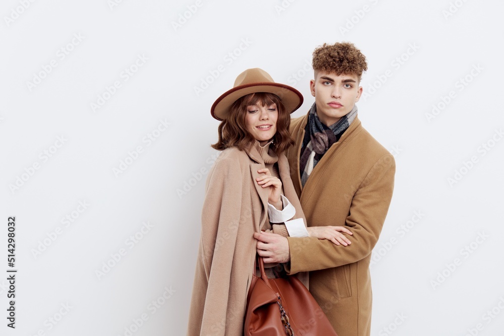 a stylish, loving couple, a man and a woman are standing on a white background in an autumn coat, and a woman is clinging to a man with her hands folded on him a stylish, loving couple, a man and a woman are standing on a white background in an autumn coat, and a woman is clinging to a man with her hands folded on him