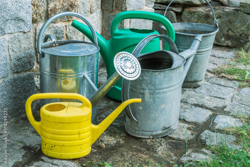 Group of garden watering can in front of stone well during drought Group of garden watering can in front of stone well during drought