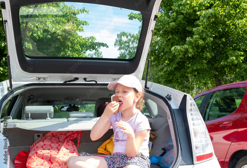 The child is hot, the girl eats ice cream and sits in the trunk of a car.