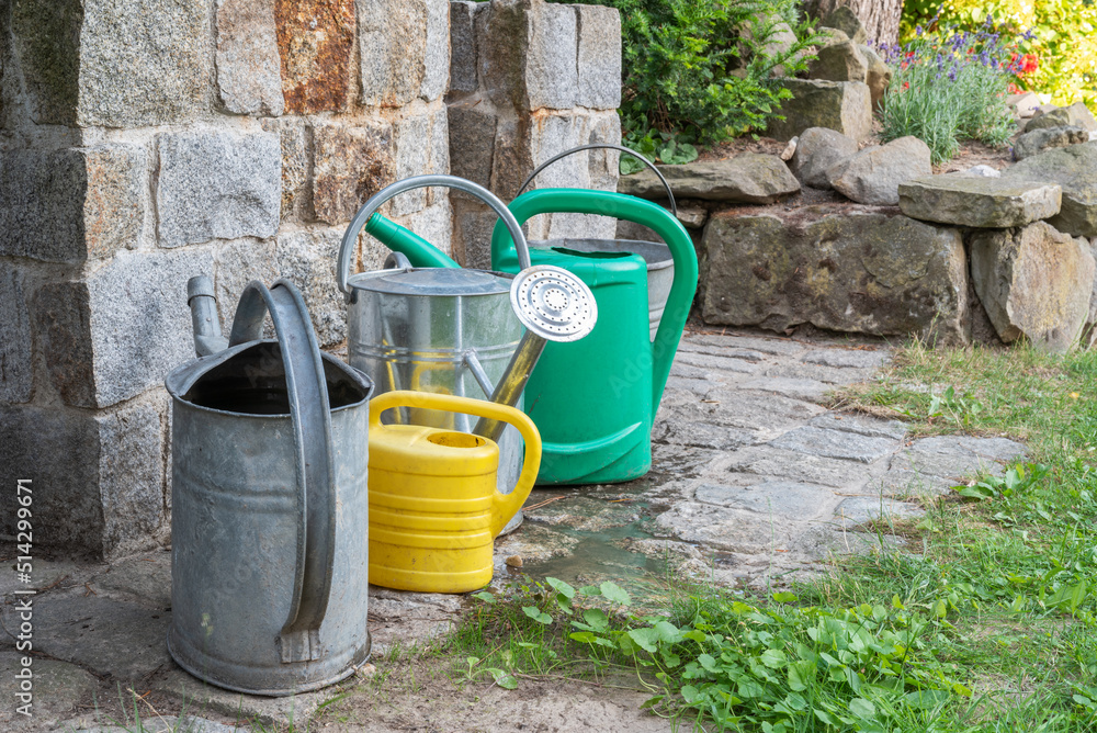 Watering cans full of water in front of stone well in garden during drought in summer Watering cans full of water in front of stone well in garden during drought in summer