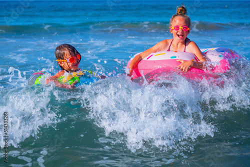 Joyful childs on inflatable rings riding on breaking wave. Travel, healthy lifestyle, swimming and summer holiday concept.