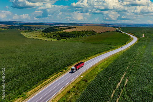 red truck driving on asphalt road along the green fields. Aerial view landscape. drone photography. cargo delivery and transportation concept