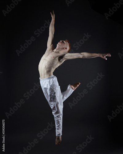 Fototapeta Naklejka Na Ścianę i Meble -  red-haired male dancer demonstrates the choreographic elements of the dance. photo shoot in the studio on a dark background