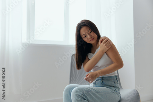 Tormented from shoulder dislocation fractures pain after lifting weights in the wrong position tanned beautiful young Asian woman touching painful shoulder at home interior living room. Cool offer