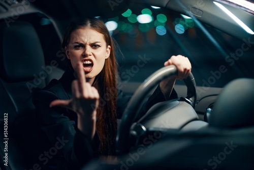 an angry, aggressive woman sits behind the wheel of a car wearing a seat belt and shows a negative gesture to the camera emotionally screaming