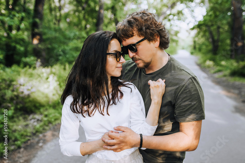 Bearded stylish man and hippie brunette woman in sunglasses hugging and smiling outdoors in the park. Portrait, photograph of people in love.