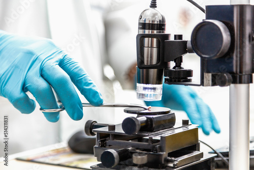 scientist holds a clamp to make an analysis in the laboratory with a microscope.