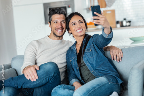 Happy young couple making a video call with smart phone while sitting on couch at home.