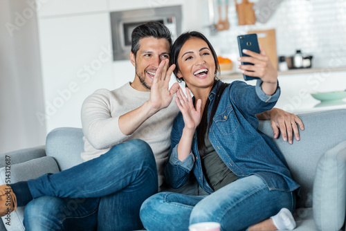 Happy young couple making a video call with smart phone while sitting on couch at home.