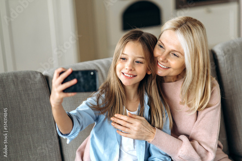 Happy smiling caucasian grandmother and granddaughter  or a mom with a daughter are taking selfie using phone  smiling happily and looking at phone camera
