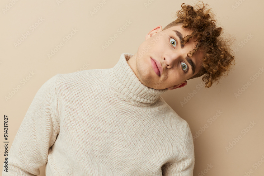 a close portrait of a handsome, funny man, with curly hair, standing on a beige background in a light turtleneck, looking pleasantly into the camera holding his head tilted a close portrait of a handsome, funny man, with curly hair, standing on a beige background in a light turtleneck, looking pleasantly into the camera holding his head tilted