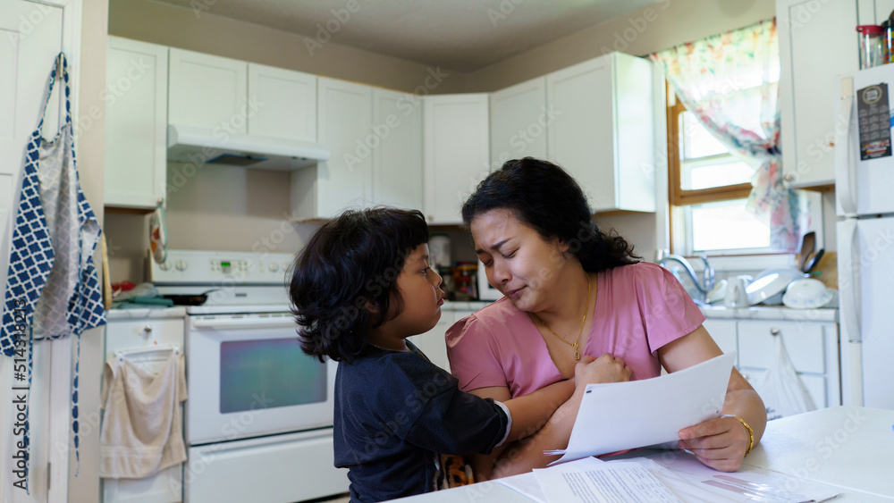 Sad daughter hugging his mother. She is young asian woman unemployed reading paper pay bills feeling frustrated of getting eviction letter or bank debt notification, concept unemployed pay bills.