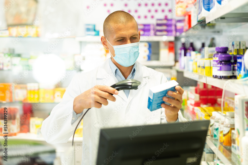 Portrait of pharmacist in medical mask working at the cash register in pharmacy - scans barcode on the medicine package