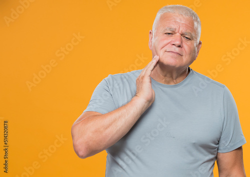 portrait of an adult man in a gray t-shirt on a yellow background isolated. an elderly man has a toothache. discomfort in the face of an older man.