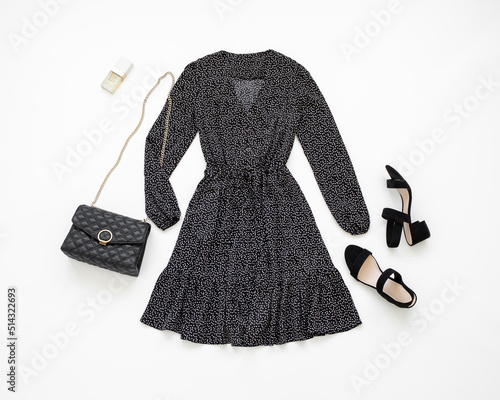 Black evening dress, small black bag with chain strap and heeled sandals on white background. Women's stylish outfit. Overhead view of woman's clothes. Flat lay, top view.