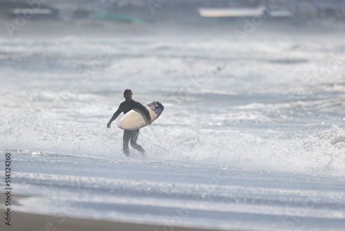 湘南の荒れた海でサーフボードを持ってビーチを歩く男性
