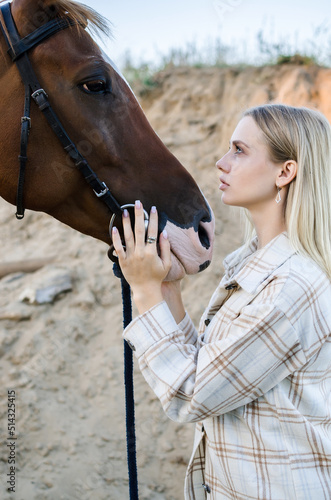 Young blonde woman hugs a horse close-up portrait outdoors in nature. Pleasure, love and care for animals, 