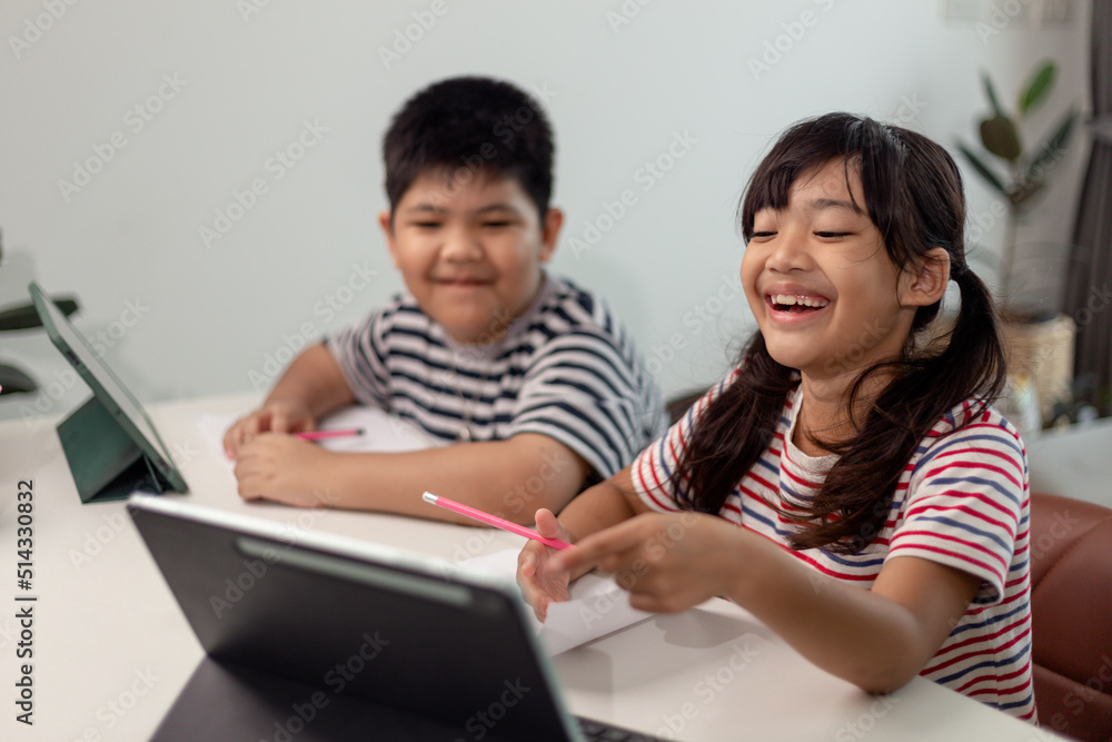 Asian boys and girls enjoy online learning by taking notes and using tablets at home. Asian boys and girls enjoy online learning by taking notes and using tablets at home.