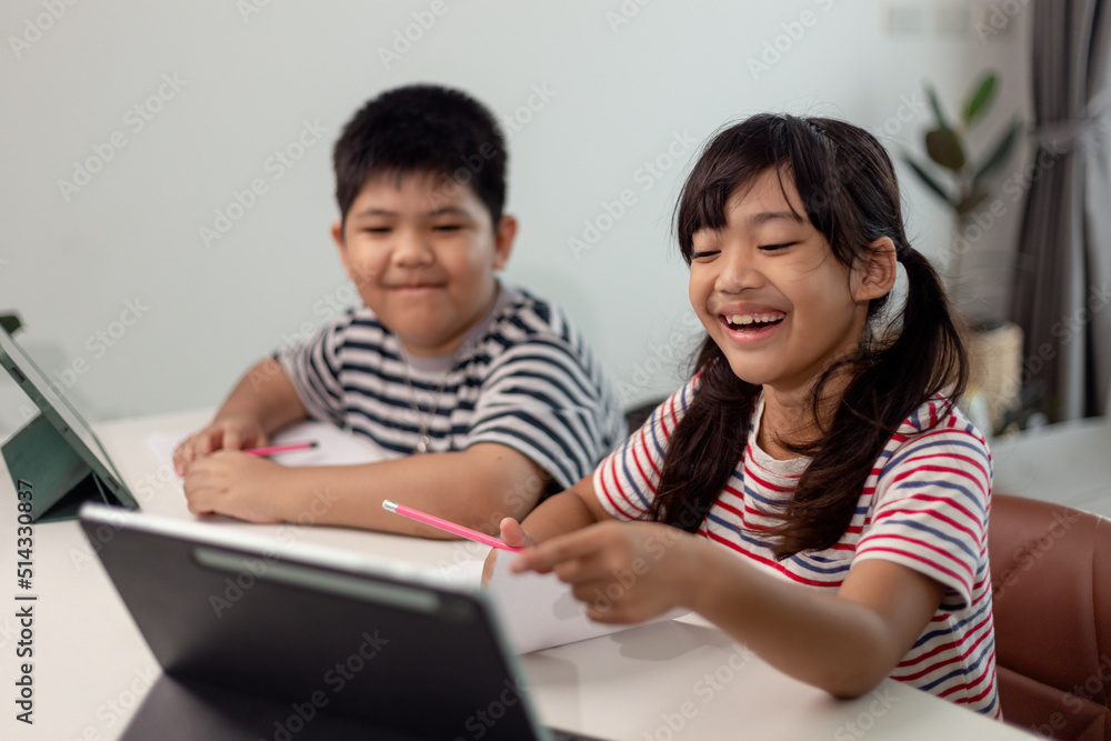 Asian boys and girls enjoy online learning by taking notes and using tablets at home. Asian boys and girls enjoy online learning by taking notes and using tablets at home.