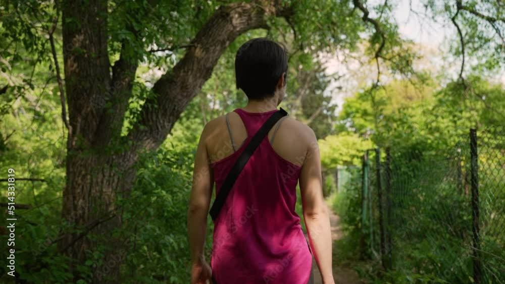 Woman wearing pink tanktop walking through a forest trail next to a fence on a sunny summer day. Slow motion. Woman wearing pink tanktop walking through a forest trail next to a fence on a sunny summer day. Slow motion.
