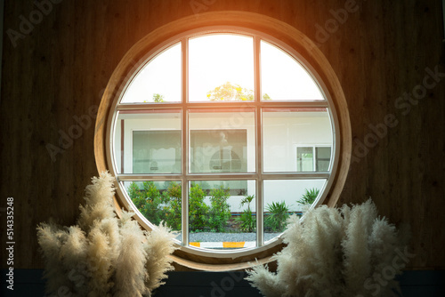 The glass circle window for to see view outside the house with white flower grass near it and sunlight to shine in.