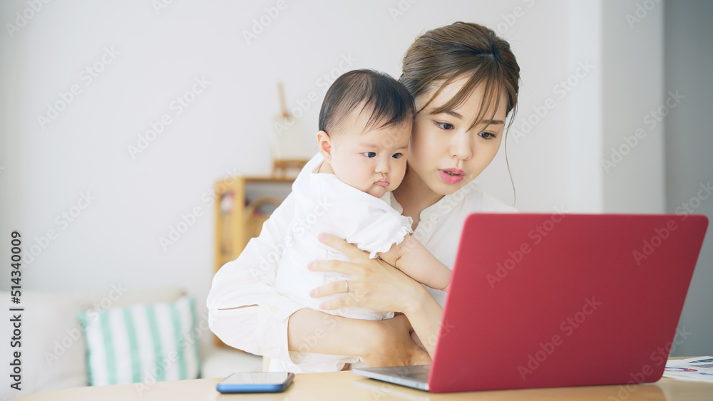 赤ちゃんを抱っこしながら自宅で仕事する女性 子育てしながらの在宅勤務 赤ちゃんを抱っこしながら自宅で仕事する女性 子育てしながらの在宅勤務