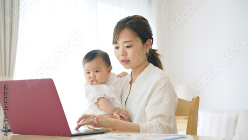 赤ちゃんを抱っこしながら自宅で仕事する女性 子育てしながらの在宅勤務