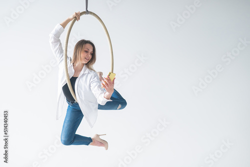Caucasian woman gymnast on an aerial hoop takes a selfie on a smartphone.  © Михаил Решетников