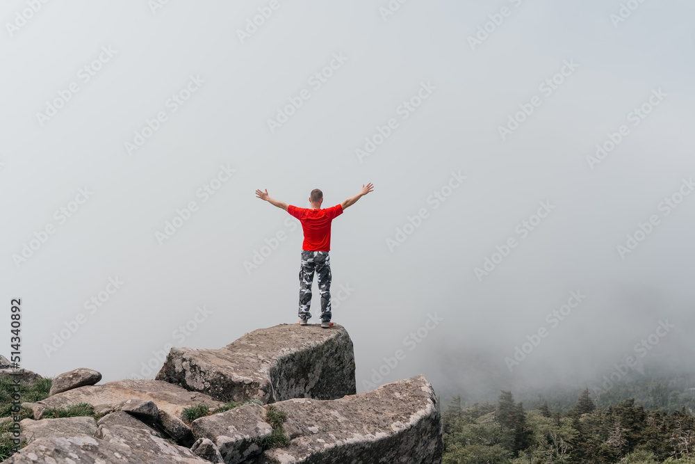 Hiker man on the top of the mountain enjoys the aerial view, raising his hands above the clouds. Mount Pidan