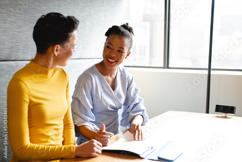 Smiling multiracial businesswomen discussing over document in creative office photo