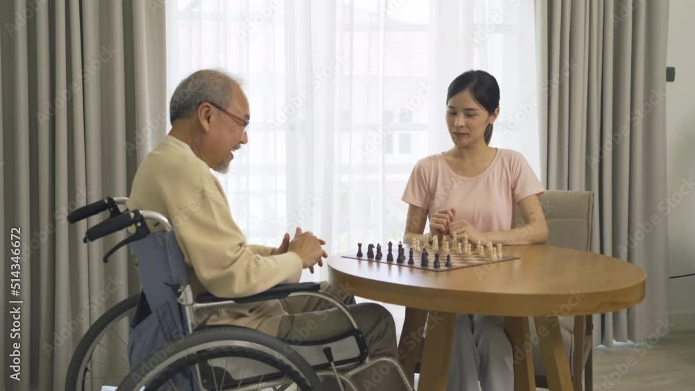 Asian daughter and old father with wheelchair, family playing a chess game together at home. People lifestyle. Activity. Therapy recover mind. Asian daughter and old father with wheelchair, family playing a chess game together at home. People lifestyle. Activity. Therapy recover mind.