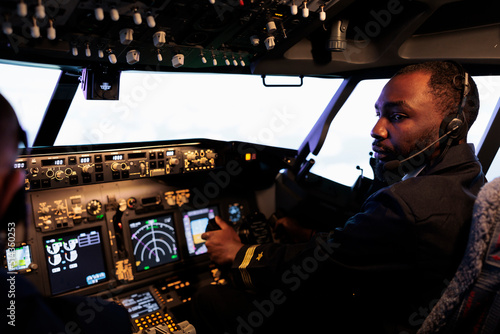 African american aviator flying plane jet in teamwork with captain, using dashboard command and navigation. Team of airliners pushing control panel buttons and lever to takeoff and fly.