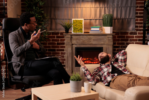 African american male therapist consulting man laying on couch, doing psychoanalysis to solve problems at therapy session. Talking about behavior issues and giving counseling advice.