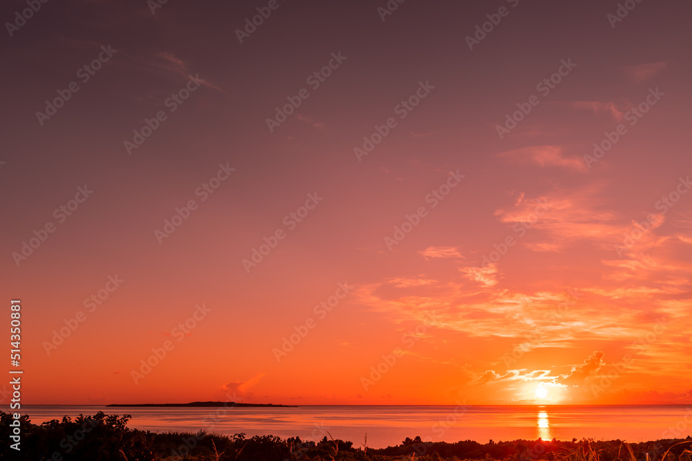 Beautiful sunrise, island on the horizon, clouds above the sun, sky and sea in pink color.